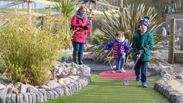 A miniature golf course with a green artificial turf, stone borders, and palm plants.