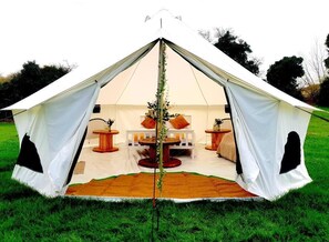 A white tent with a central table and two side tables, surrounded by a grassy field.