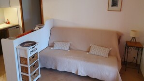 Un salon chaleureux avec un canapé beige, une petite table d’appoint avec une lampe, un meuble blanc avec des rangements et un luminaire fixé au mur.