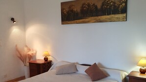 Une chambre à coucher avec un lit, deux tables de chevet, une lampe, un tableau et un vase contenant des plumes d’herbe des pampas.