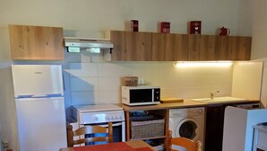 Une cuisine compacte équipée d’un réfrigérateur, d’un four à micro-ondes, d’une cuisinière et d’un évier. On y trouve une table à manger avec des chaises et un set de table rouge.