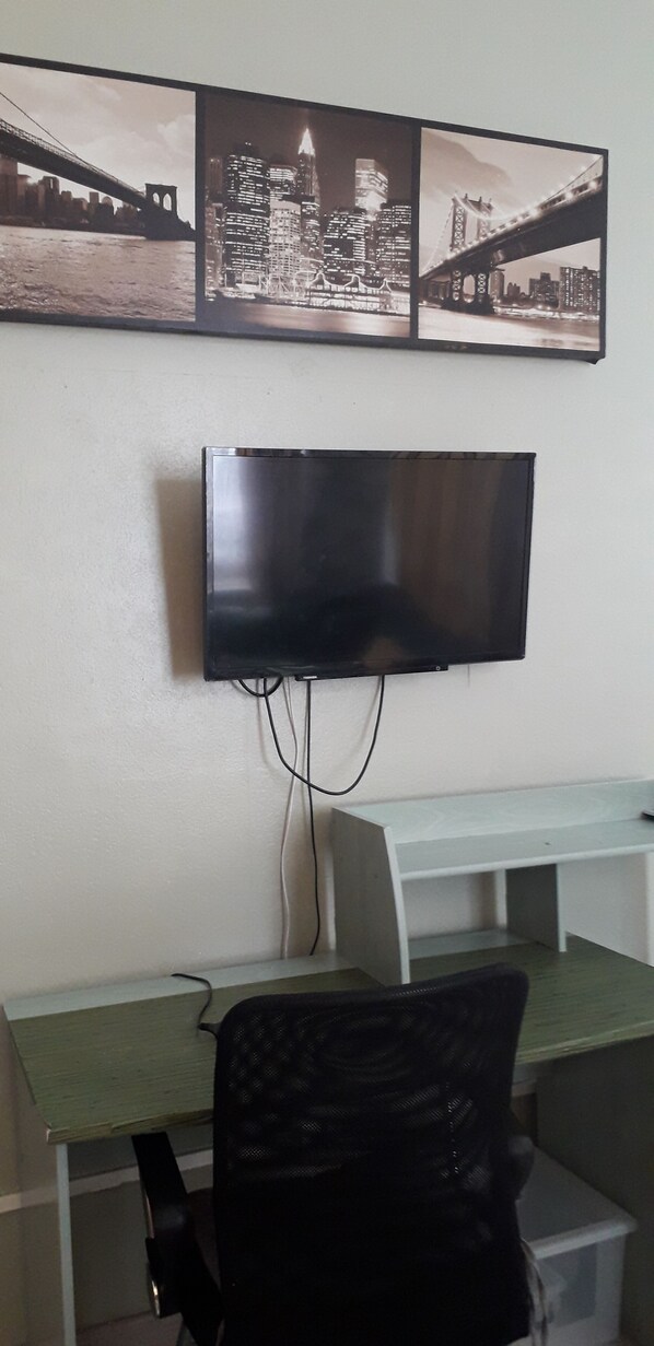Une chambre dotée d’un téléviseur à écran plat fixé au mur, d’un bureau avec une chaise et d’une petite table.