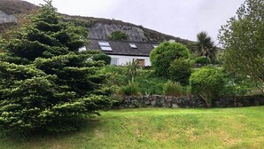 Een huis met een schuin dak, omringd door een verzorgde tuin met verschillende struiken en bomen.