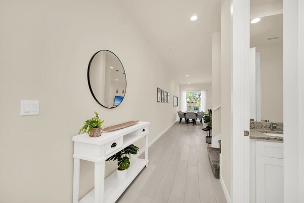 A hallway with a white console table, a mirror, and framed pictures on the wall. - Enchanted Home Near Disney (Kissimmee)