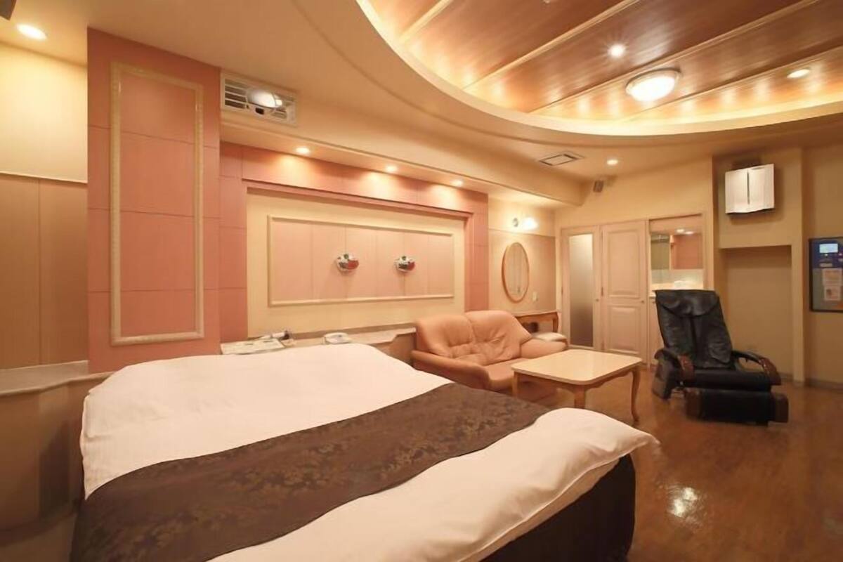 Una habitación de hotel con una cama grande, una mesita pequeña, una silla y un sillón de masaje.