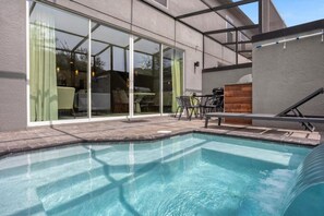 A swimming pool with a patio area, including a table and chairs, and a glass door leading to an indoor space. - Themed Home Near Disney w/Pool (Kissimmee)