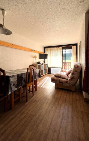 A dining area with a table and chairs, a television, and a window with curtains.