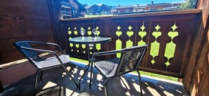 A balcony with two metal chairs and a small round table, a wooden fence with a geometric pattern, and a view of buildings in the background. - Ground floor, balcony, tv, ski locker, 25m², Les Gets (Les Gets)