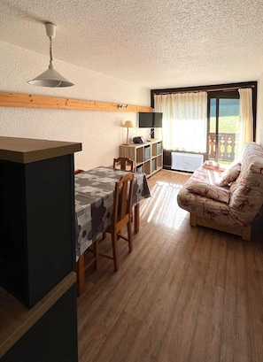 Um quarto aconchegante com uma mesa de jantar, cadeiras, um sofá, uma televisão e uma janela com cortinas.