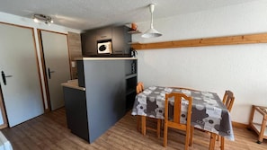 A compact kitchen with a microwave, a wooden dining table with chairs, and a white ceiling light.
