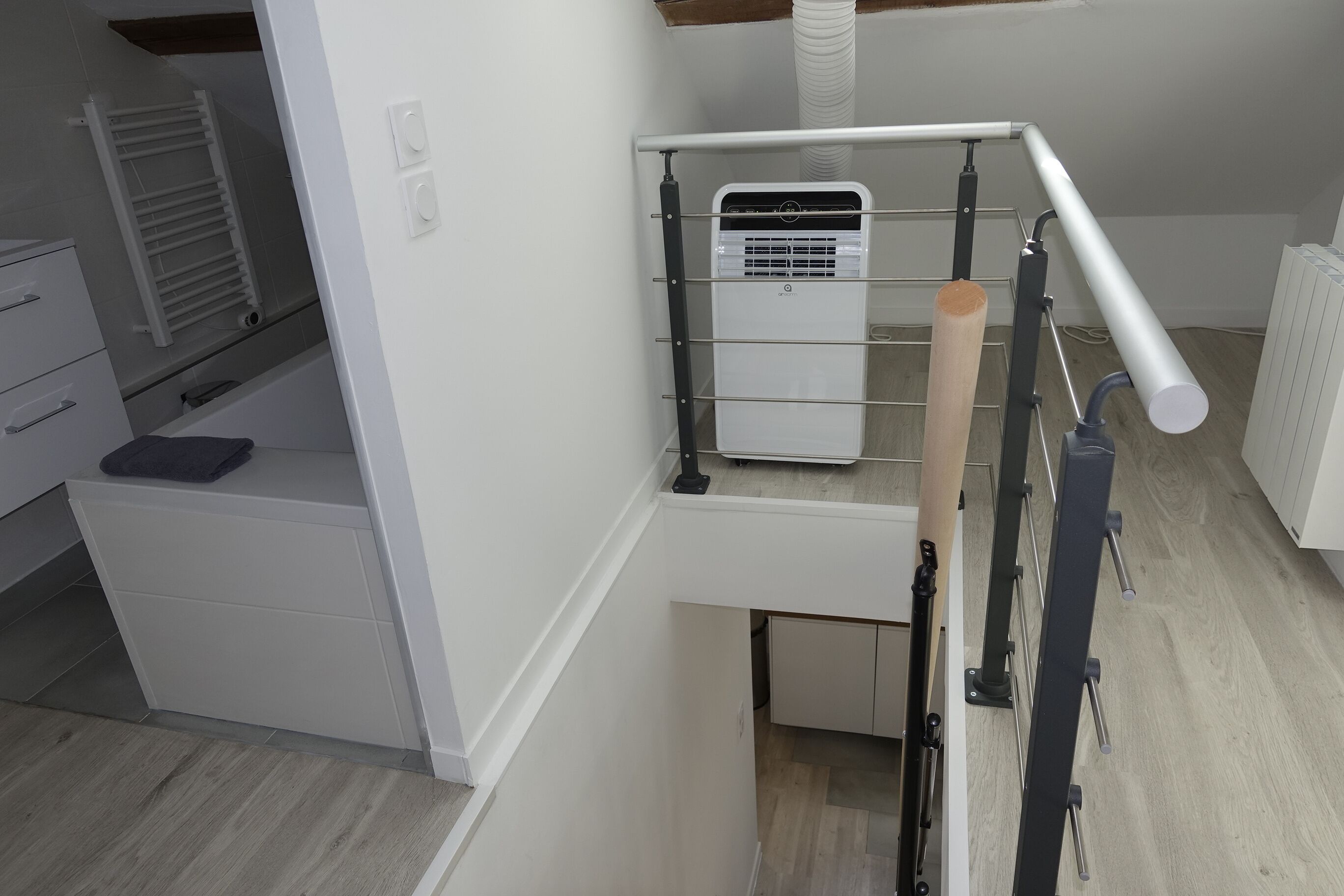 Una cocina compacta con aire acondicionado integrado, un taburete de madera y un armario blanco.