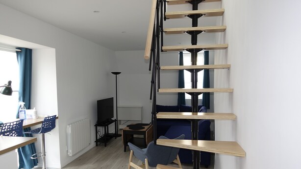A modern living room with a spiral staircase, a dining area with bar stools, and a seating area with a sofa and chairs. - Dijon : Superbe Appartement Hyper Centre en Duplex (Dijon)