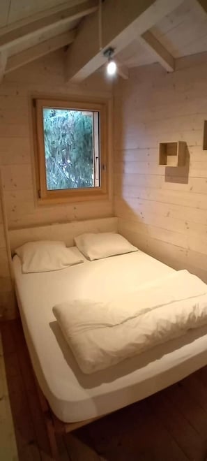 A wooden-paneled room with a bed, a window, and a ceiling fan.