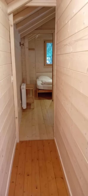 A narrow wooden hallway leading to a bedroom with a window and a radiator.