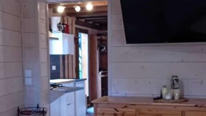 A wooden dining table with chairs, a kitchen area with cabinets, and a flat-screen TV mounted on the wall. - Chalet, 350m from ski slopes, parking, tv, 104m², Les Gets (Les Gets)