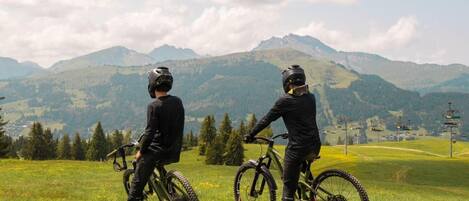 Deux cyclistes sur un champ herbeux, avec une chaîne de montagnes en arrière-plan.