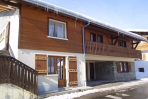Une maison en bois à deux étages, dotée d’un balcon, de volets en bois et de fondations en pierre.