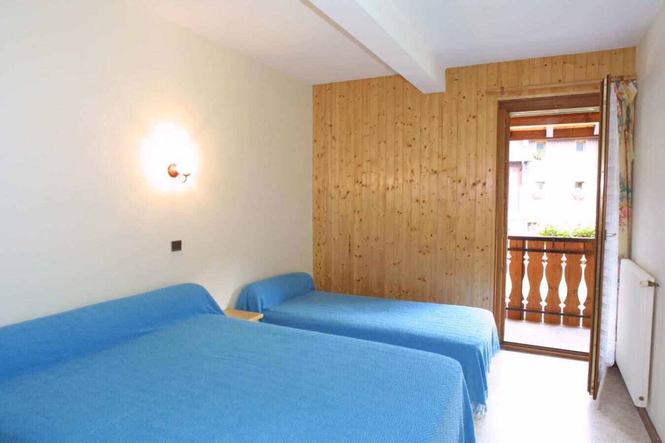 Una habitación con dos camas, paredes de madera, un balcón con barandilla y una lámpara en la pared.