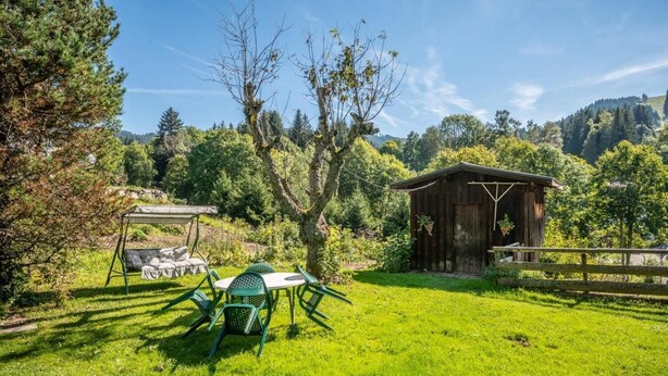 Un espacio al aire libre con césped, una caseta de madera, un conjunto de columpios y una mesa de picnic.
