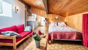 Un dormitorio acogedor con techo de madera, una cama con colcha estampada, un sofá rojo y una pequeña cocina al fondo.