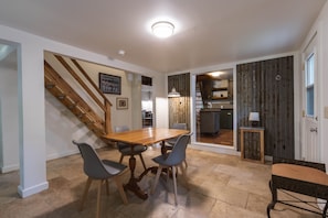 A dining area with a wooden table and chairs, a staircase, and a kitchen visible through an open door. - Quaint cottage in the woods with swim spa (Frazeysburg)