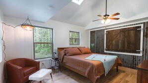 Une chambre à coucher comprenant un lit, une chaise, un bureau, un ventilateur de plafond et de grandes fenêtres.
