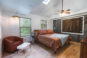 A bedroom with a bed, a chair, a desk, a ceiling fan, and large windows. - Quaint cottage in the woods with swim spa (Frazeysburg)
