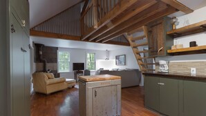Un vaste espace de vie doté d’un plancher en bois, d’un canapé, d’une kitchenette équipée d’une machine à café et d’un escalier.