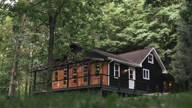 Une cabane en bois, située dans une forêt, avec une façade en bois et un toit en pente.