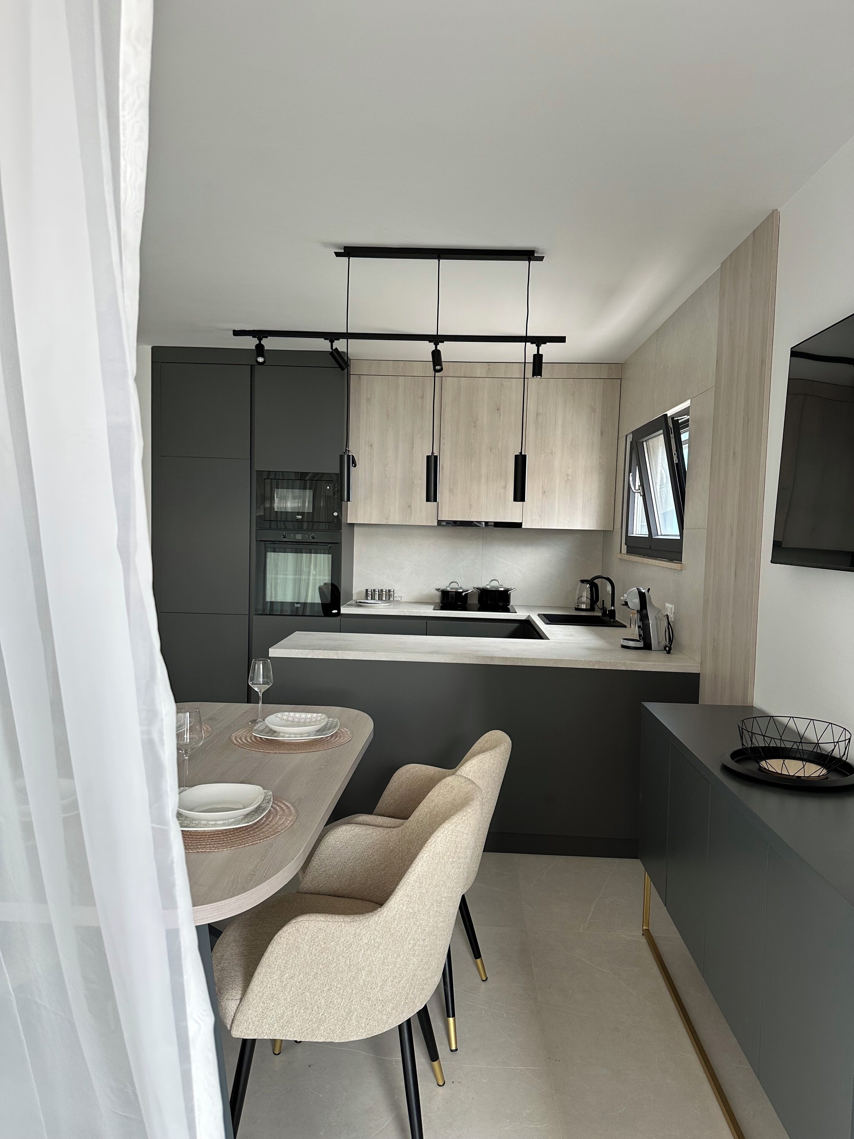 A modern kitchen with a central island, pendant lighting, and a dining area with chairs and a table.