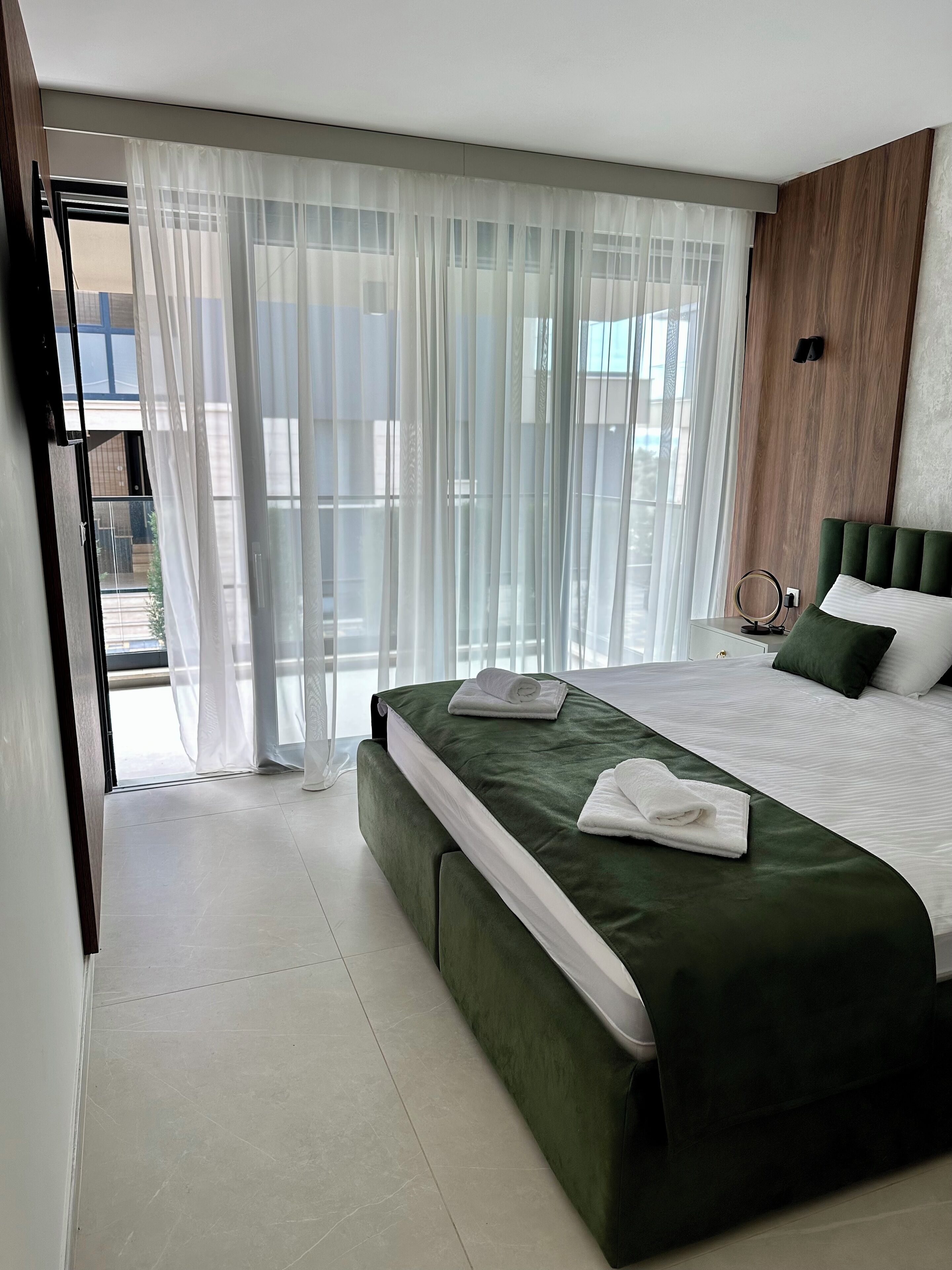 Un dormitorio moderno con una cama grande, ropa de cama verde y cortinas traslúcidas.