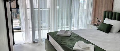 Un dormitorio moderno con una cama grande, ropa de cama verde y cortinas traslúcidas.