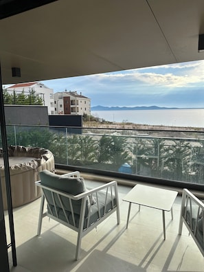 A balcony with a view of a body of water and distant mountains. There are two chairs and a small table on the balcony. - Zados Luxury Residence (Zadar)