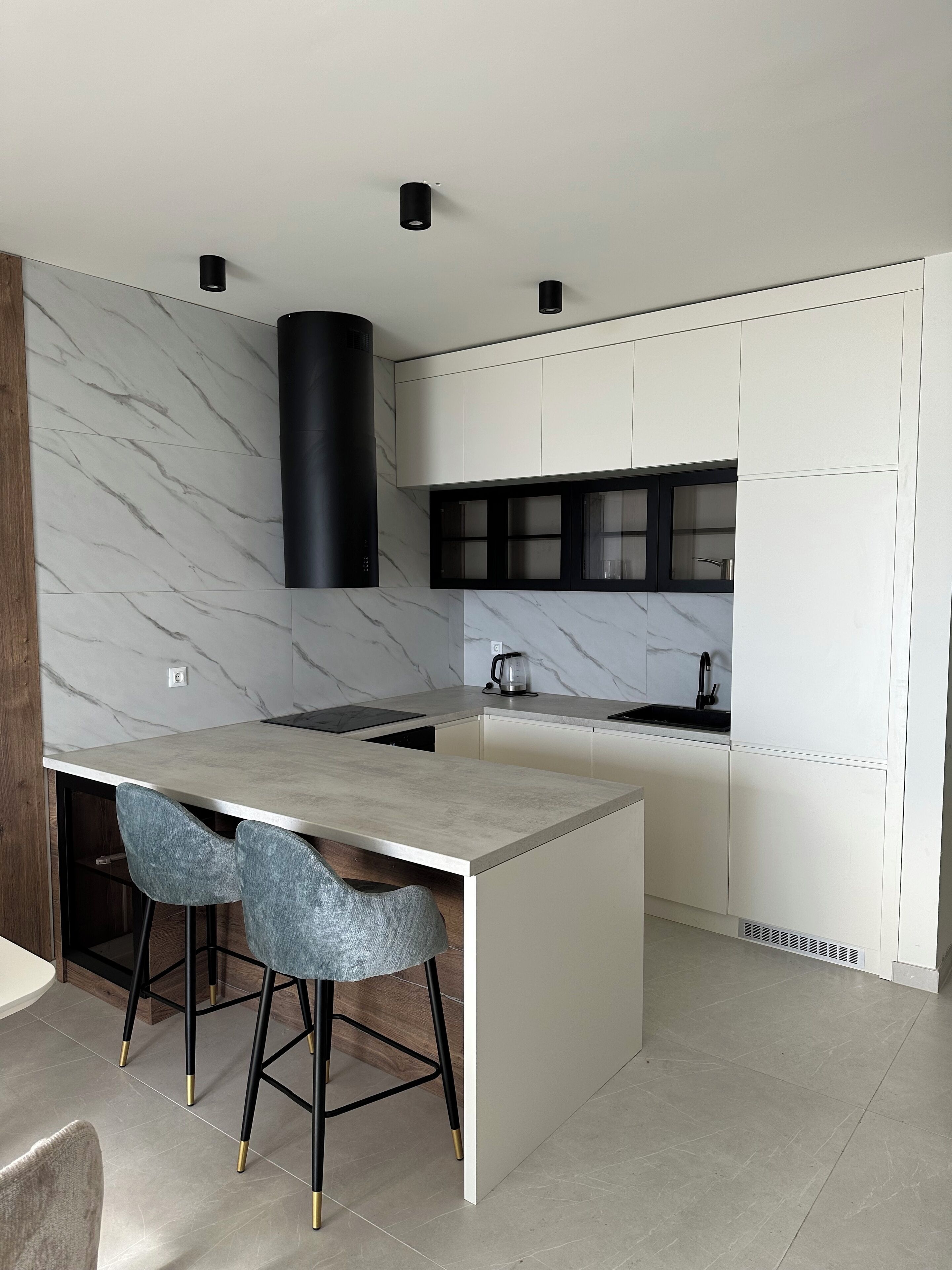 A modern kitchen with a marble backsplash, a central island with bar stools, and a black range hood.