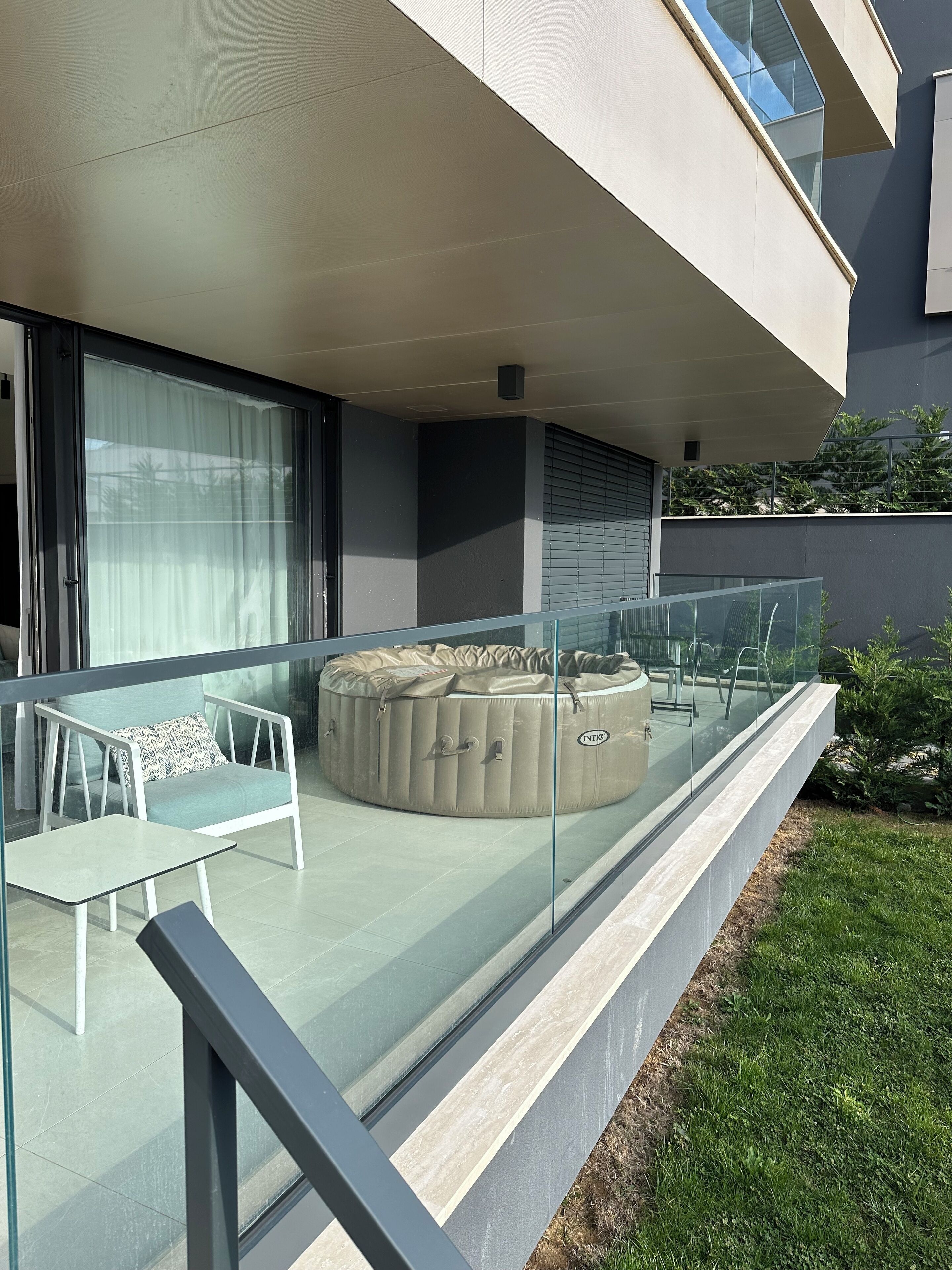 A modern outdoor seating area with a glass balustrade, a cushioned bench, and a small table.
