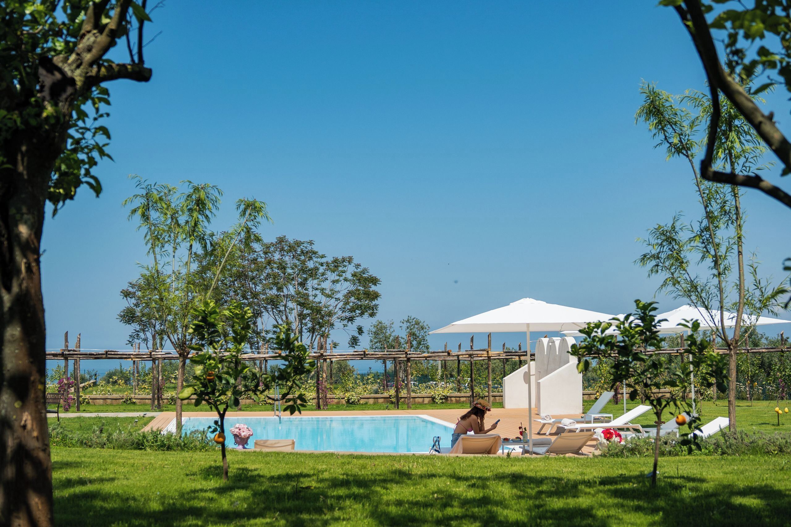 A pool area with lounge chairs and a covered seating area, surrounded by greenery and trees.