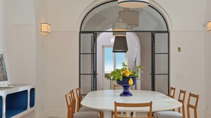 A dining area with a round table, wooden chairs, a vase with flowers, and a modern pendant light. - Tenuta Sirignano Villa Nord e Sud (Massa Lubrense)