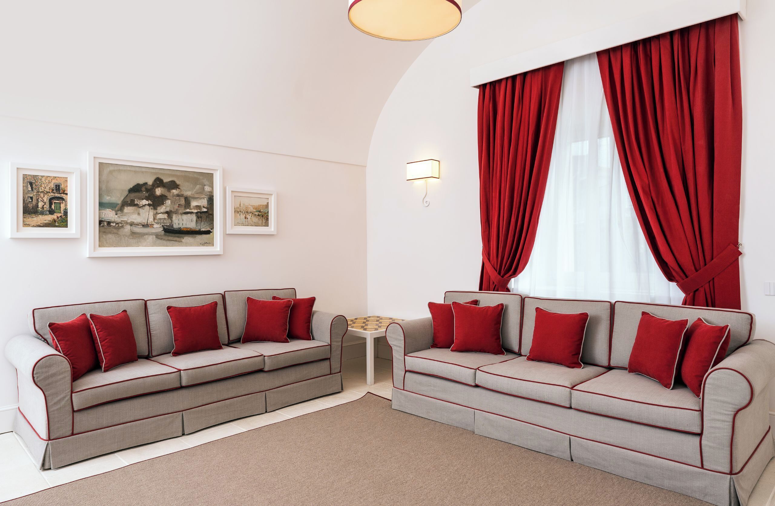 Een moderne woonkamer met twee grijze banken met rode accenten, een klein wit bijzettafeltje en drie ingekaderde kunstwerken aan de muur.