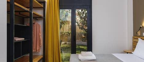 Un dormitorio con una cama, una estantería de madera, una cortina amarilla y vistas a un jardín a través de un ventanal.