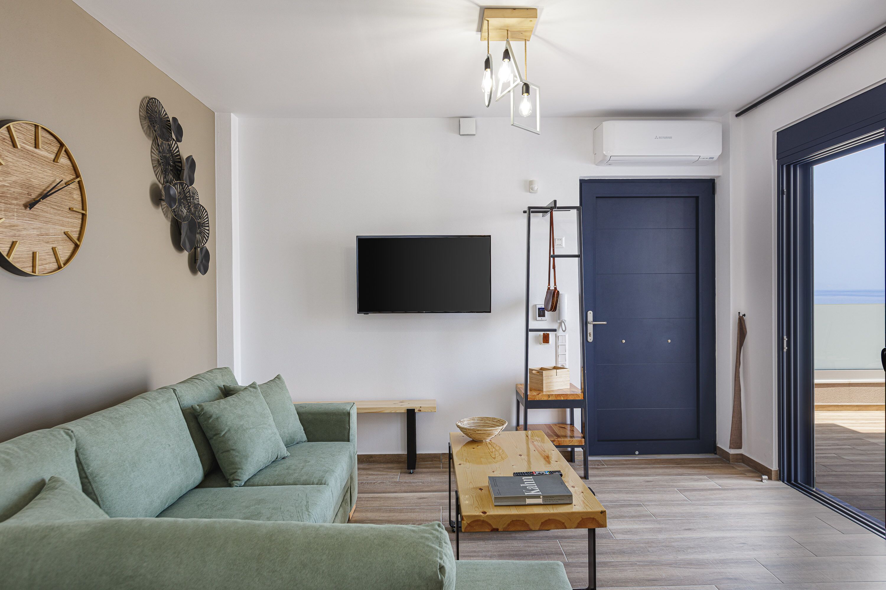 A modern living room with a green sofa, a wooden coffee table, a flat-screen TV, and a dark blue door leading to an outdoor area.