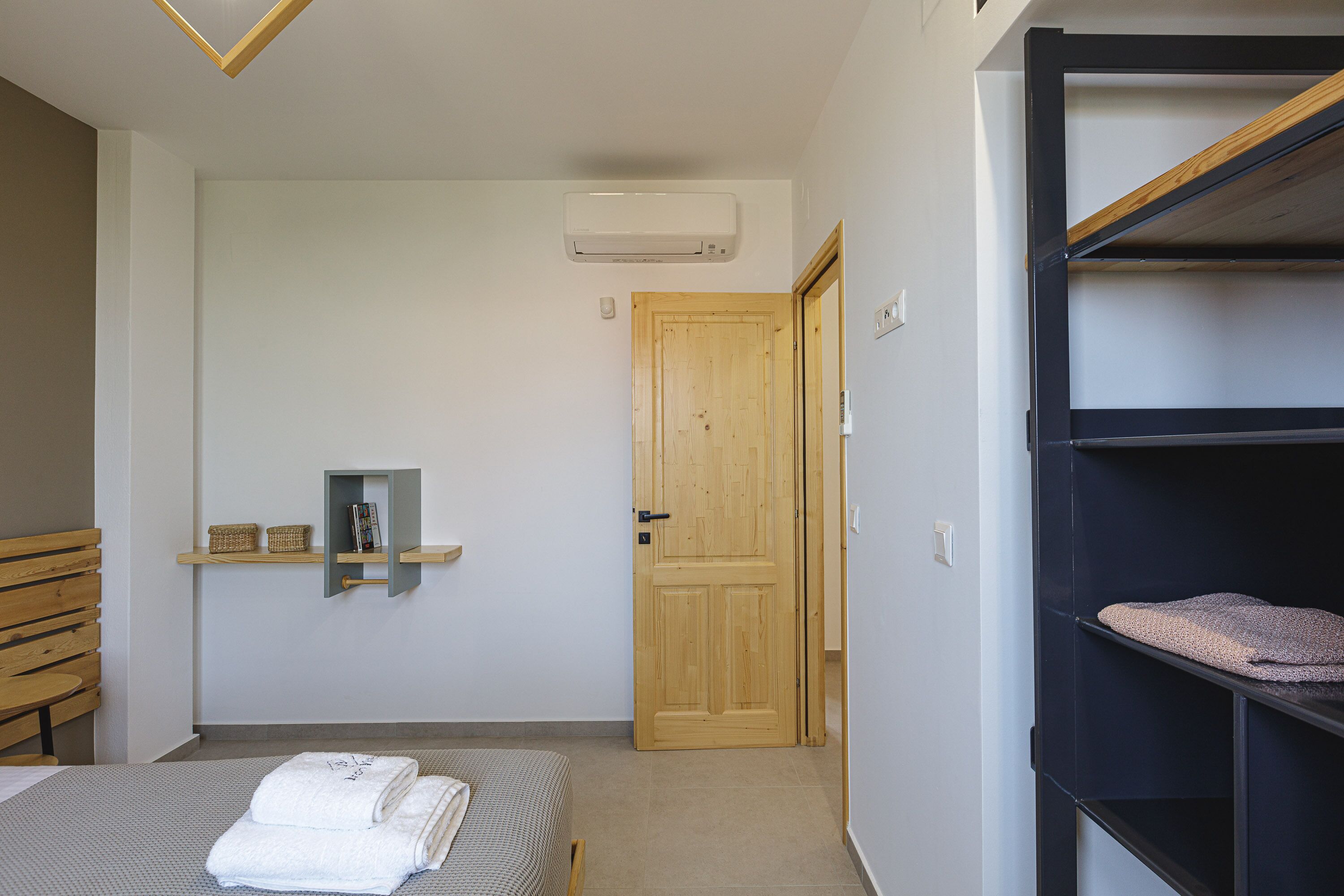 Une chambre à coucher avec un lit, une porte en bois, une étagère avec des paniers et une étagère noire avec une couverture.