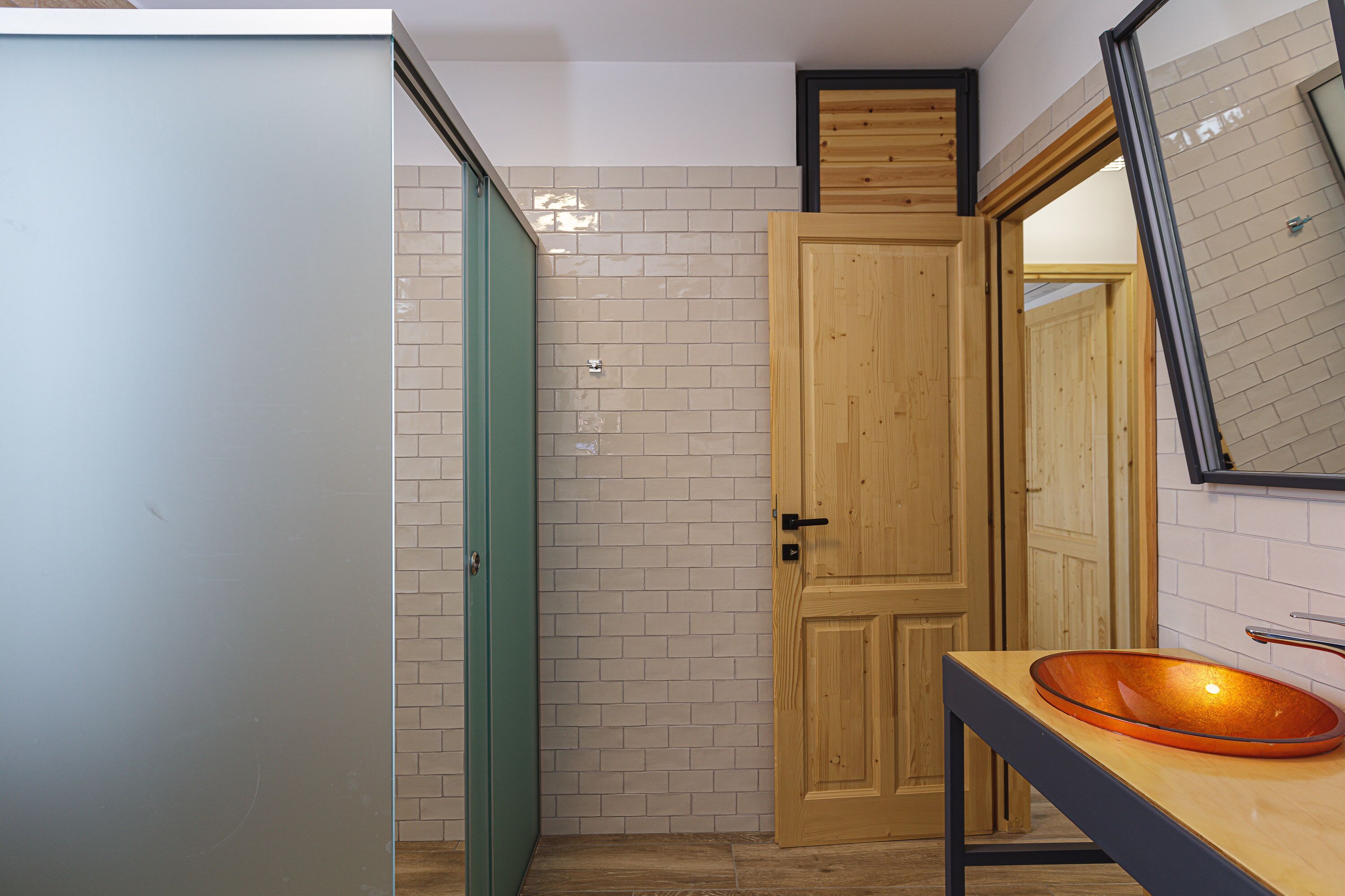 A bathroom with a wooden door, a tiled wall, and a sink with a glass basin.