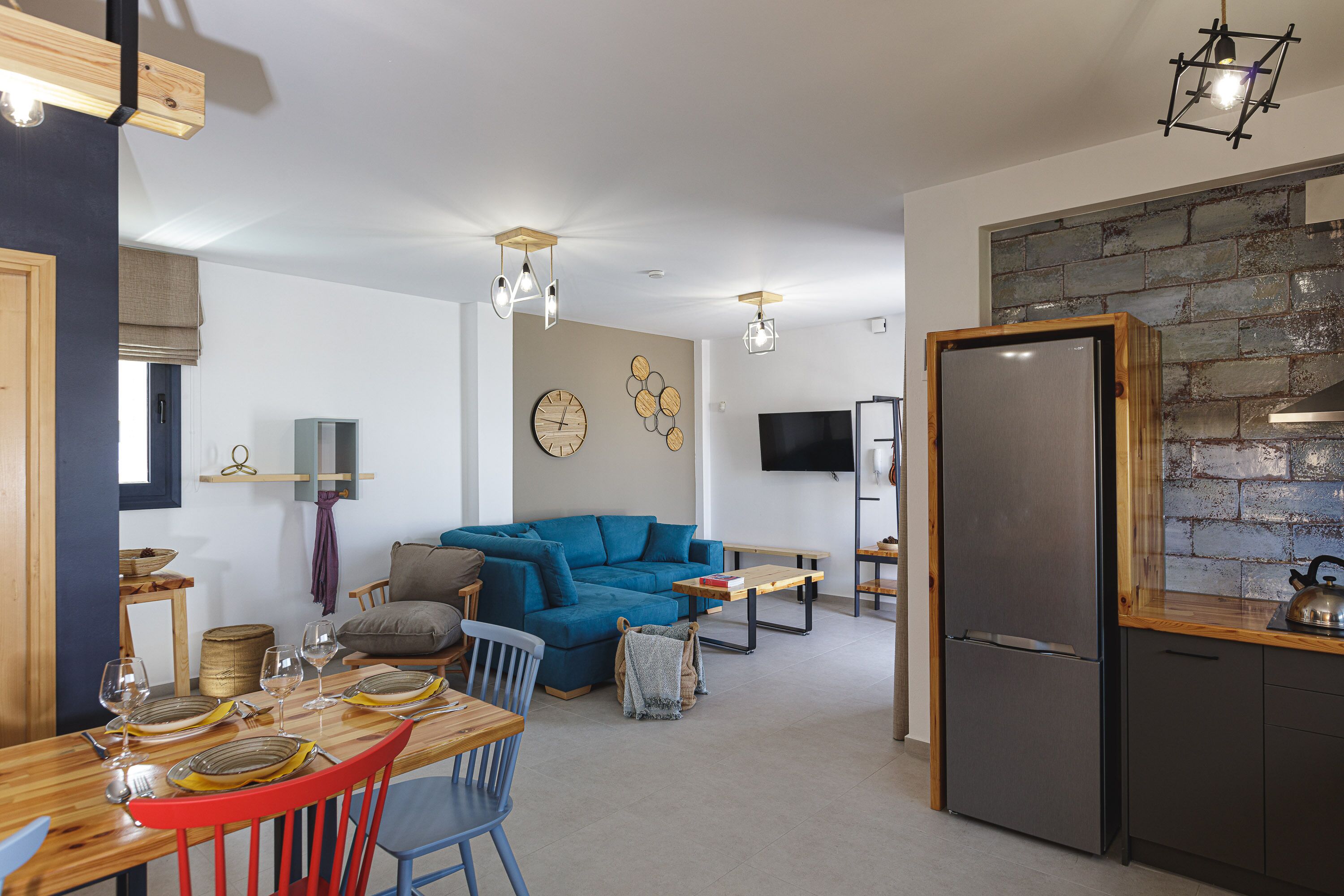 Een moderne woonkamer met een blauwe bank, een houten eettafel en een geïntegreerde keuken met een koelkast.