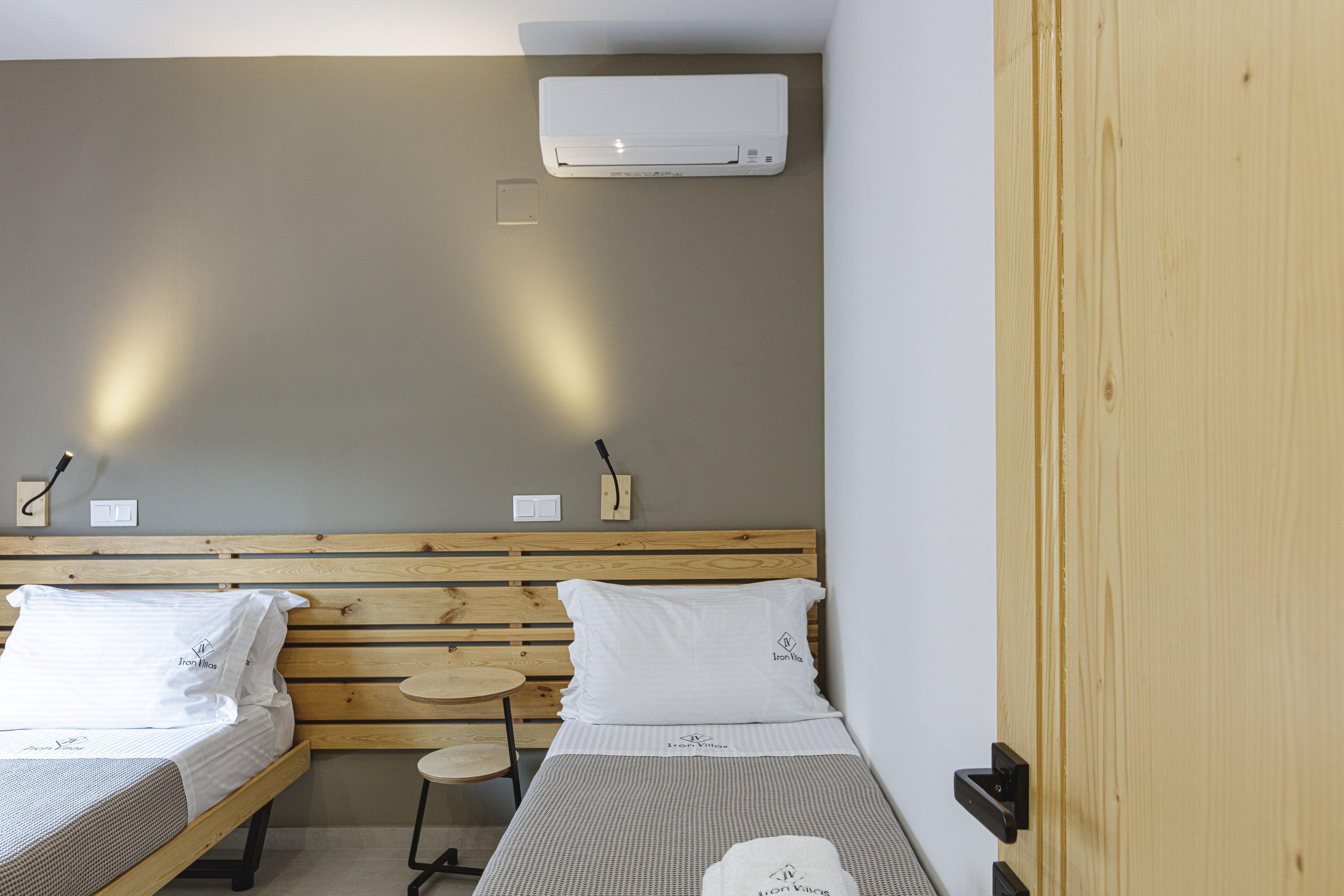 Ein Hotelzimmer mit zwei Betten, einem Holz-Kopfteil, einem kleinen runden Tisch und einer an der Wand befestigten Klimaanlage.