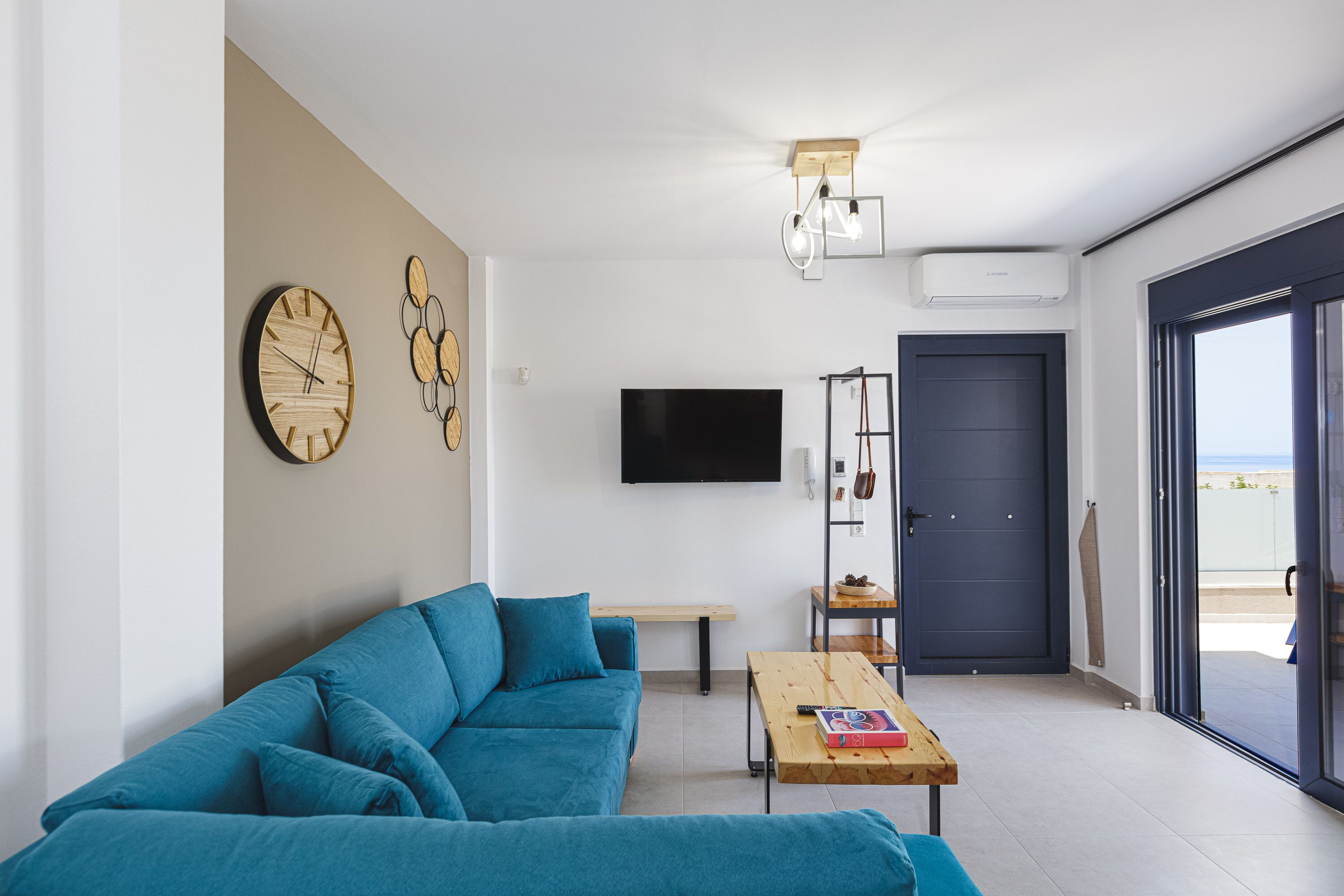 A modern living room with a blue sofa, a wooden coffee table, a flat-screen TV, and a door leading to an outdoor area.