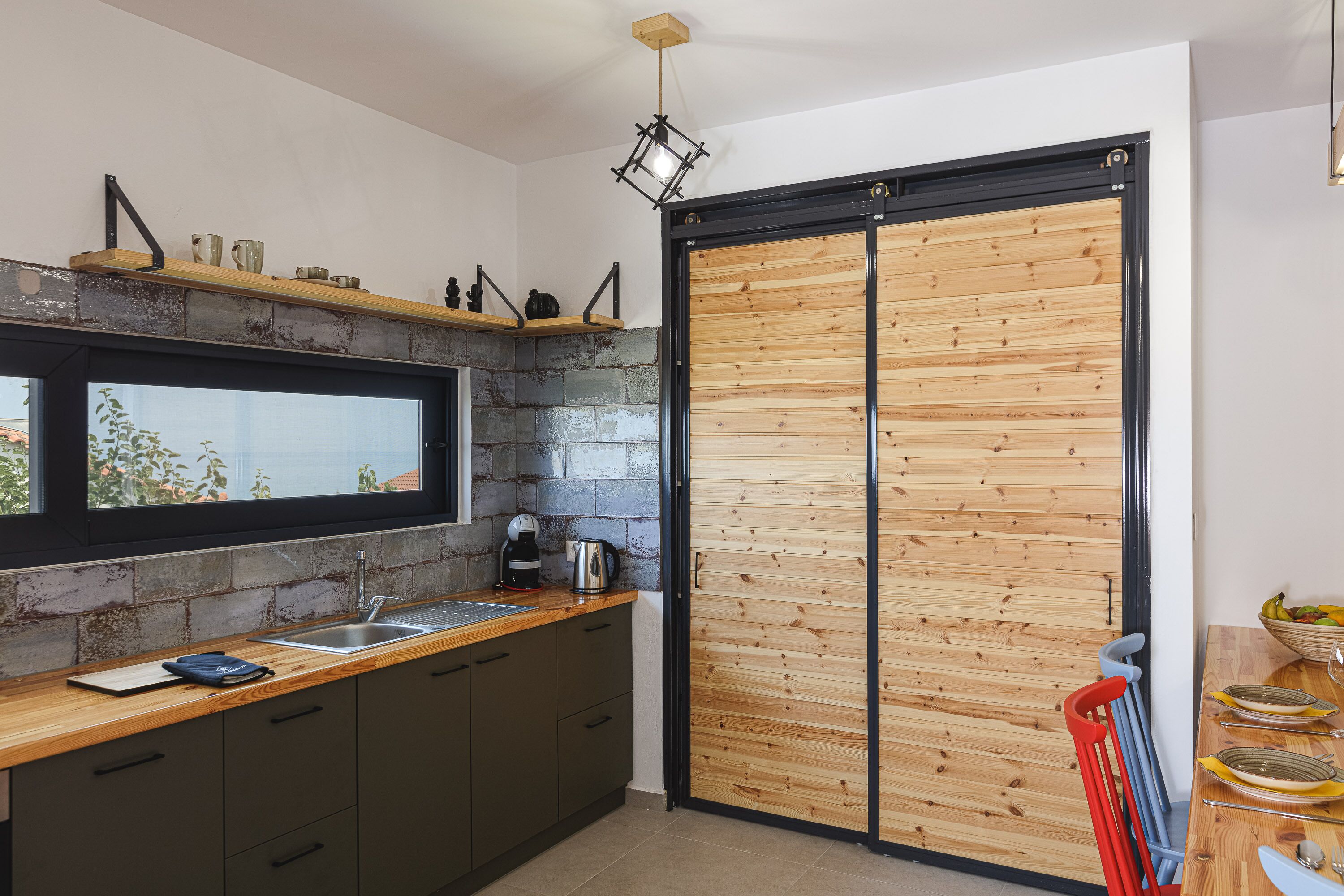 A modern kitchen with a large window, a sink, and a wooden door.