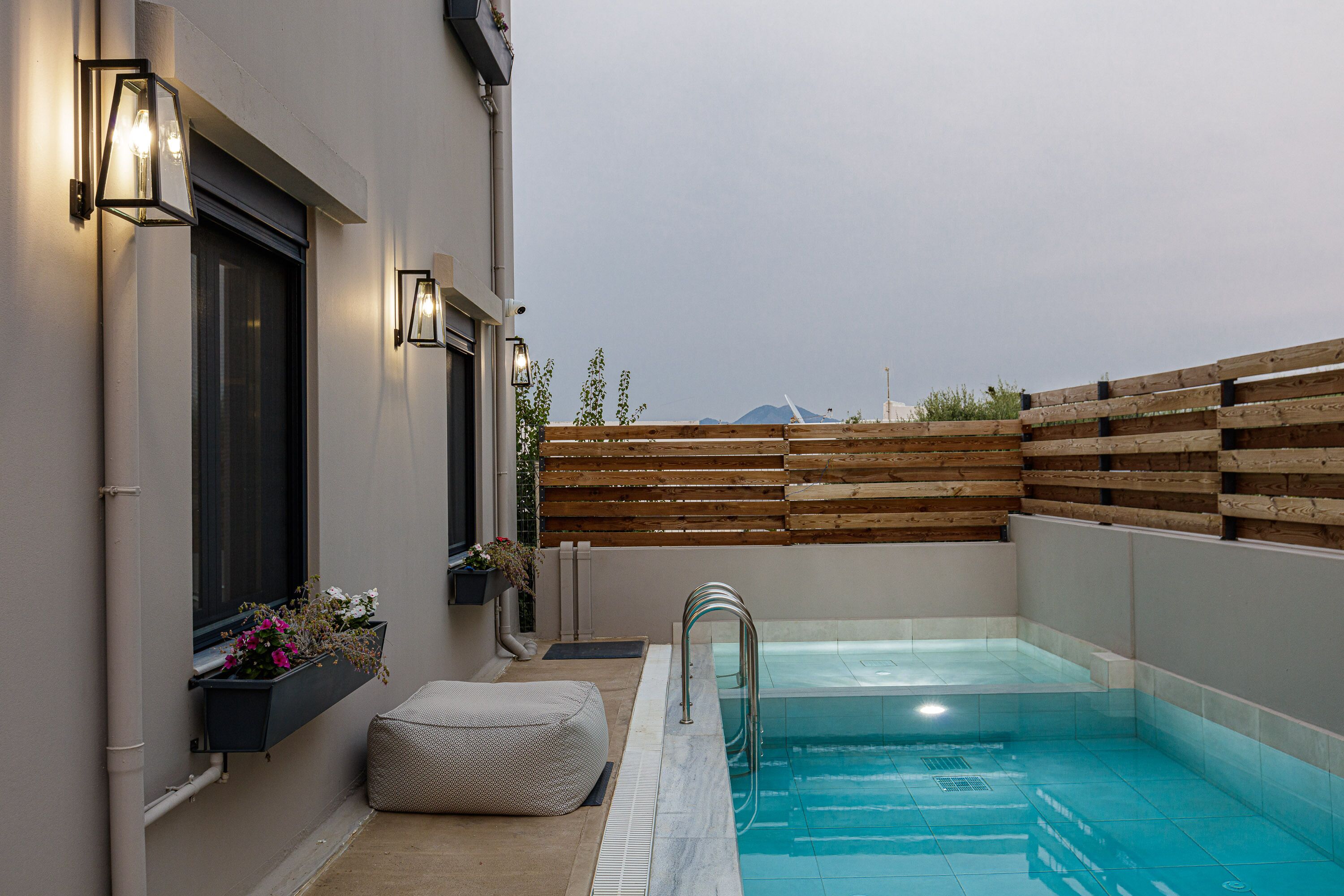 Ein moderner Poolbereich im Freien mit Holzzaun, einer Bank und einem kleinen Blumenbeet.