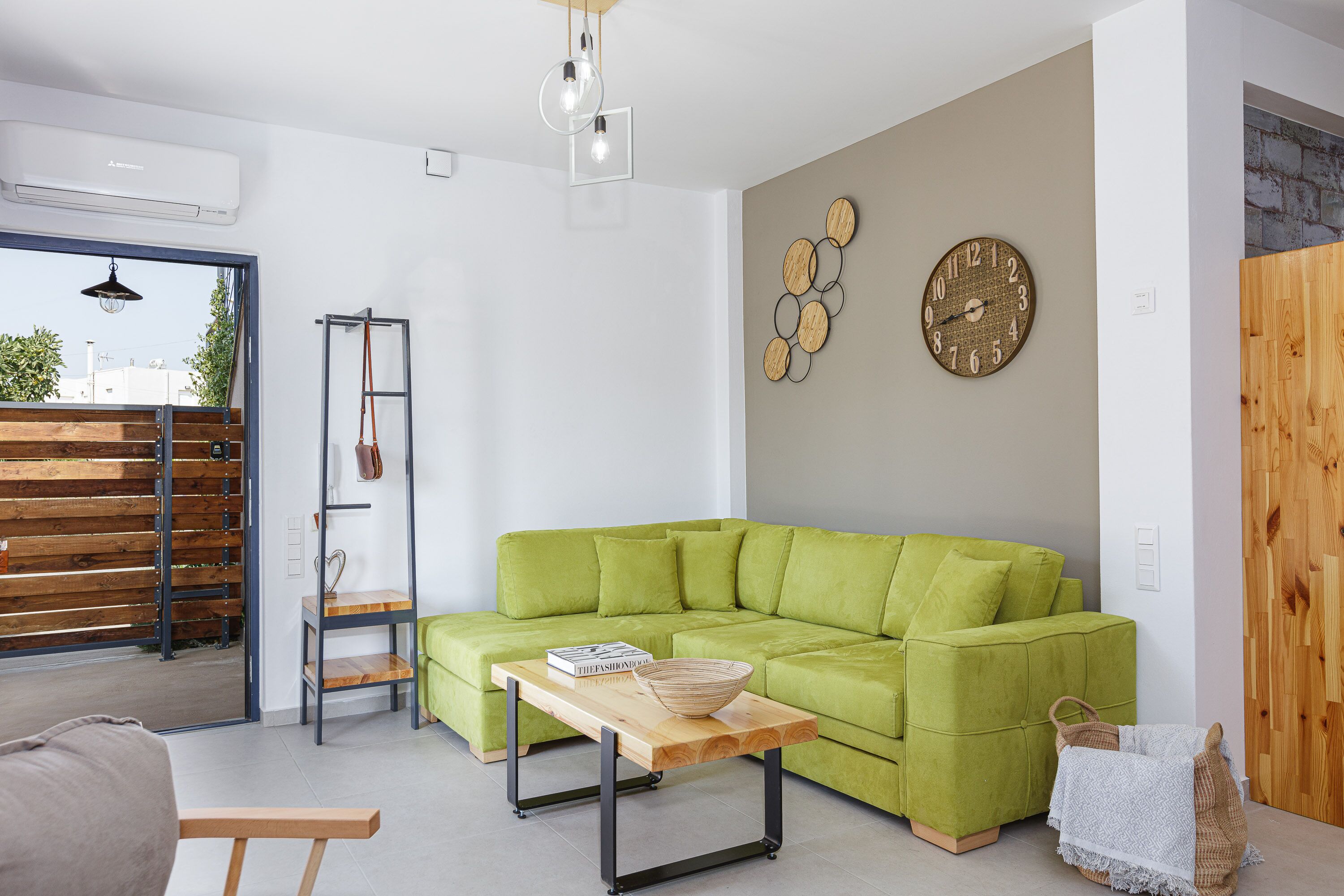A modern living room with a green sofa, a wooden coffee table, and a wall clock.
