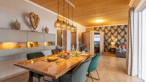 Une cuisine moderne avec un plafond en bois, des luminaires suspendus et un coin repas comprenant une longue table et des chaises.