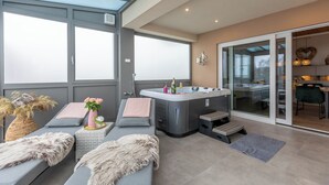 Un espace spa moderne doté d’un jacuzzi, de sièges et d’une porte vitrée donnant sur une cuisine.
